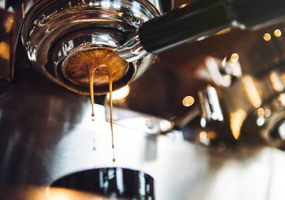 Fresh and hot espresso coffee pours from a portafilter on a nice chrome espresso machine.  Horizontal image with copy space.